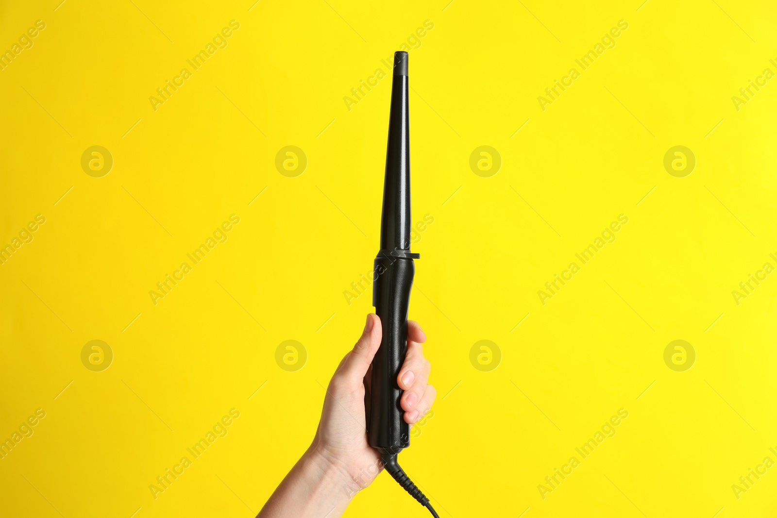 Photo of Woman holding clipless curling hair iron on yellow background, closeup