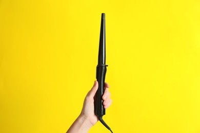 Woman holding clipless curling hair iron on yellow background, closeup