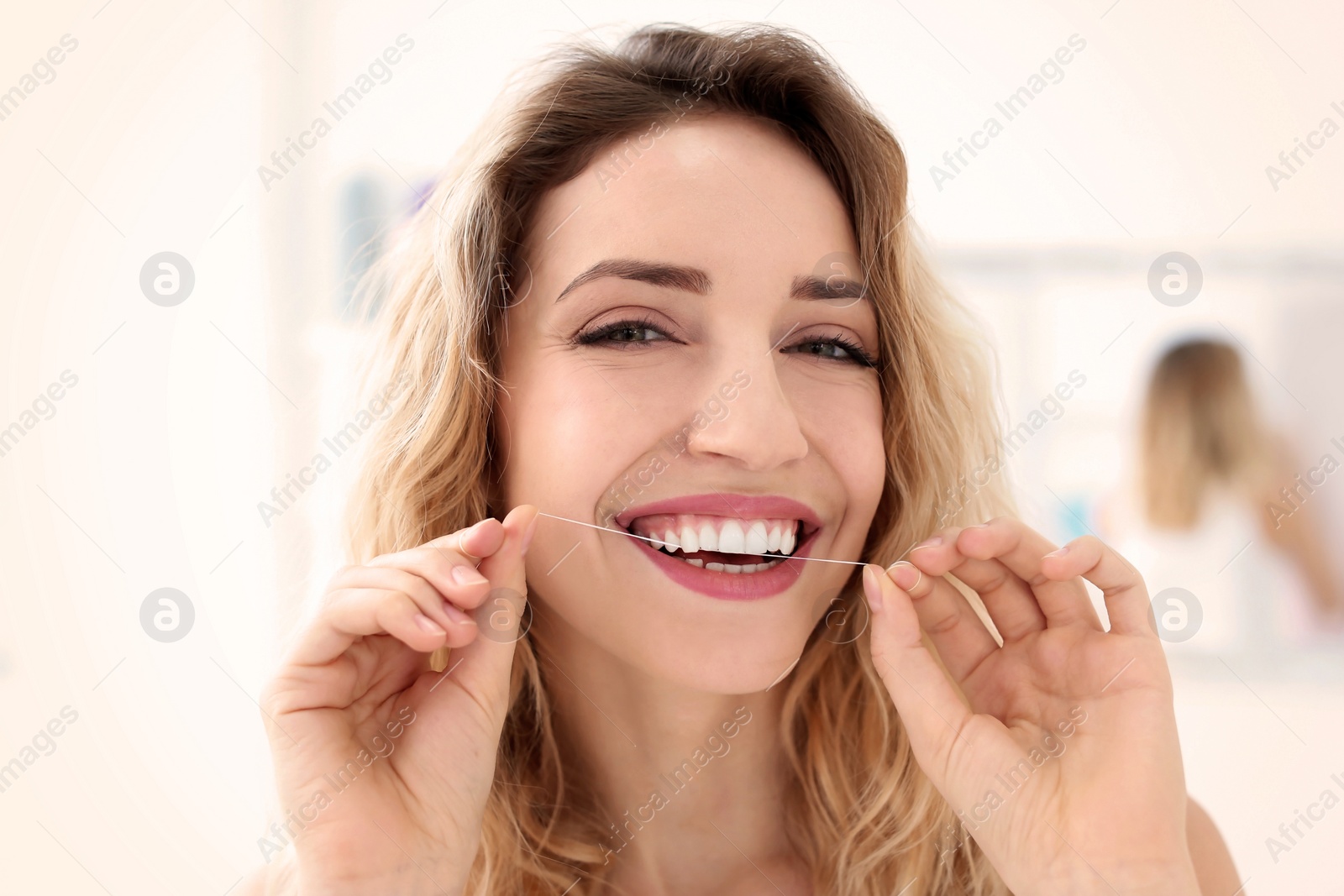 Photo of Young woman flossing her teeth indoors