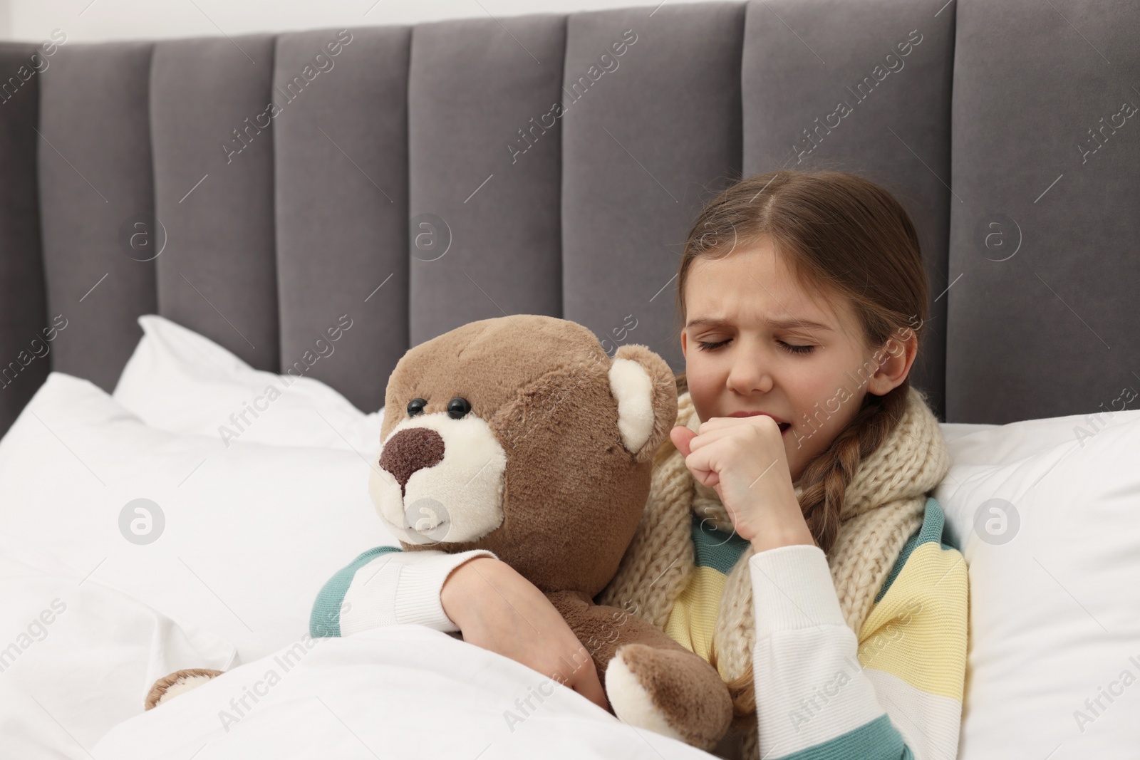 Photo of Sick girl with teddy bear coughing on bed at home