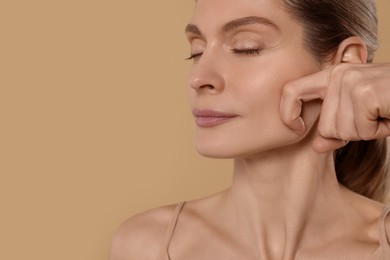 Photo of Woman massaging her face on beige background. Space for text