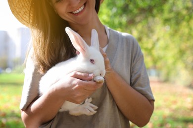 Happy woman holding cute white rabbit in park, closeup