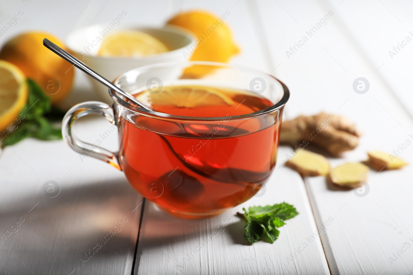 Photo of Cup of delicious ginger tea and ingredients on white wooden table, closeup