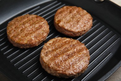 Photo of Grill pan with tasty fried hamburger patties on wooden table, closeup