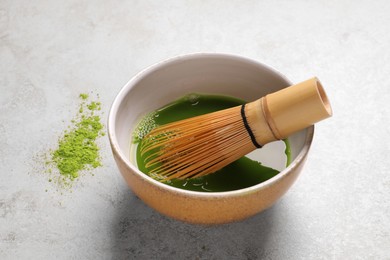 Bowl of fresh matcha tea with bamboo whisk and powder on light table, closeup