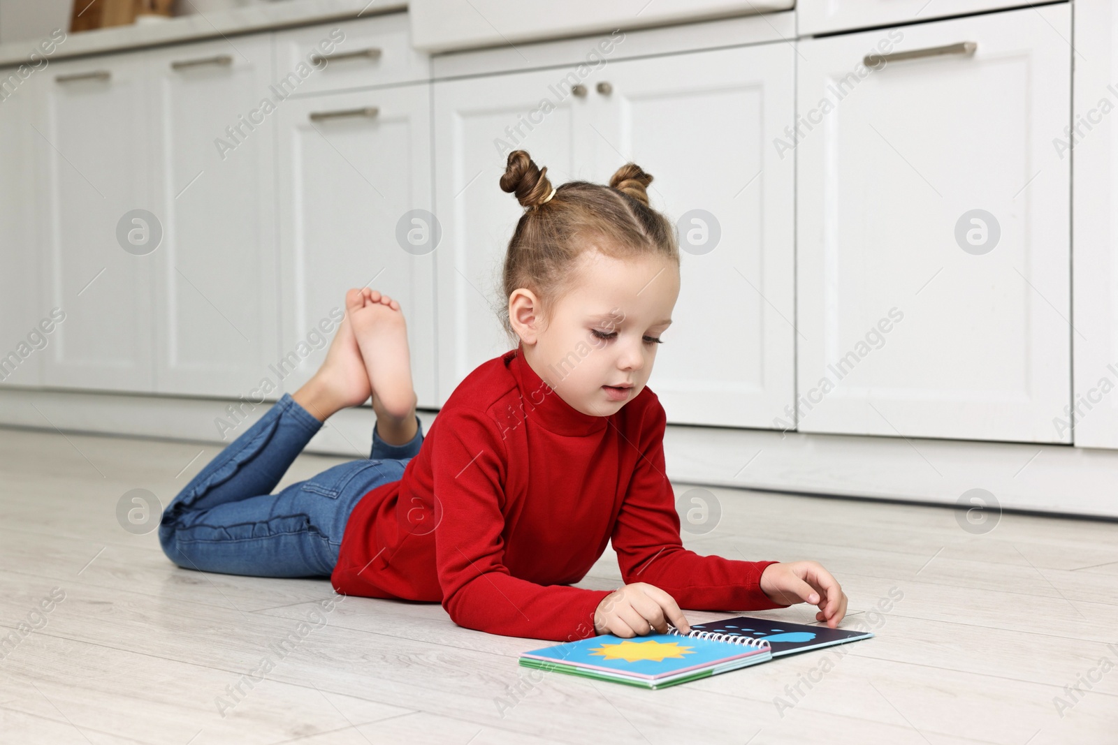 Photo of Cute little girl reading book on warm floor in kitchen. Heating system