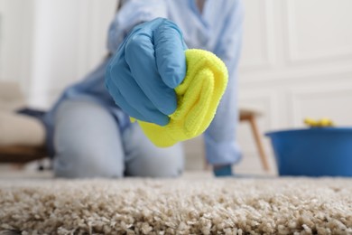 Woman in rubber gloves cleaning carpet with rag indoors, closeup. Space for text