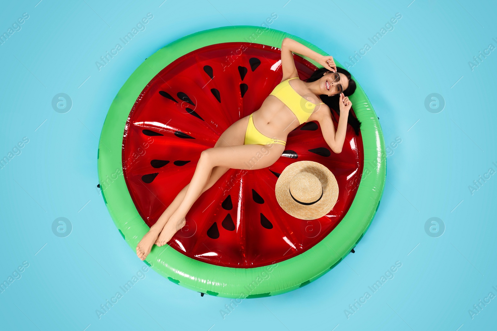 Photo of Young woman with stylish sunglasses on inflatable mattress against light blue background, above view