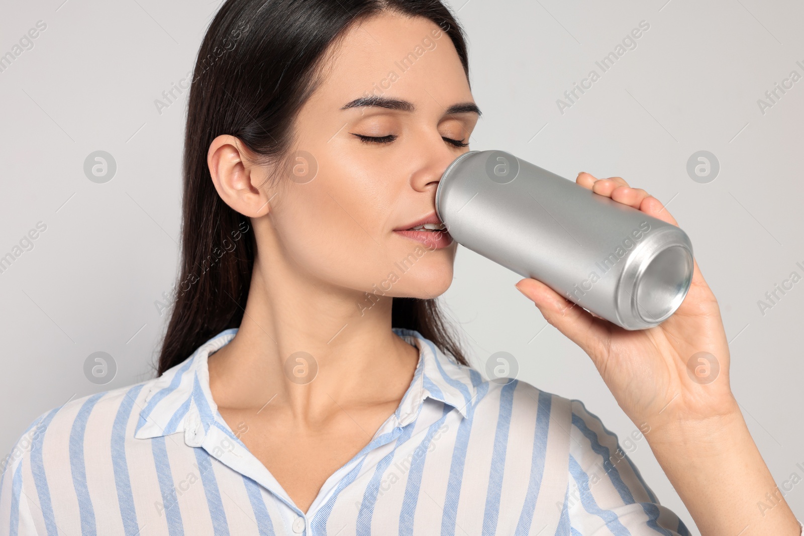 Photo of Beautiful young woman drinking from tin can on light grey background, closeup