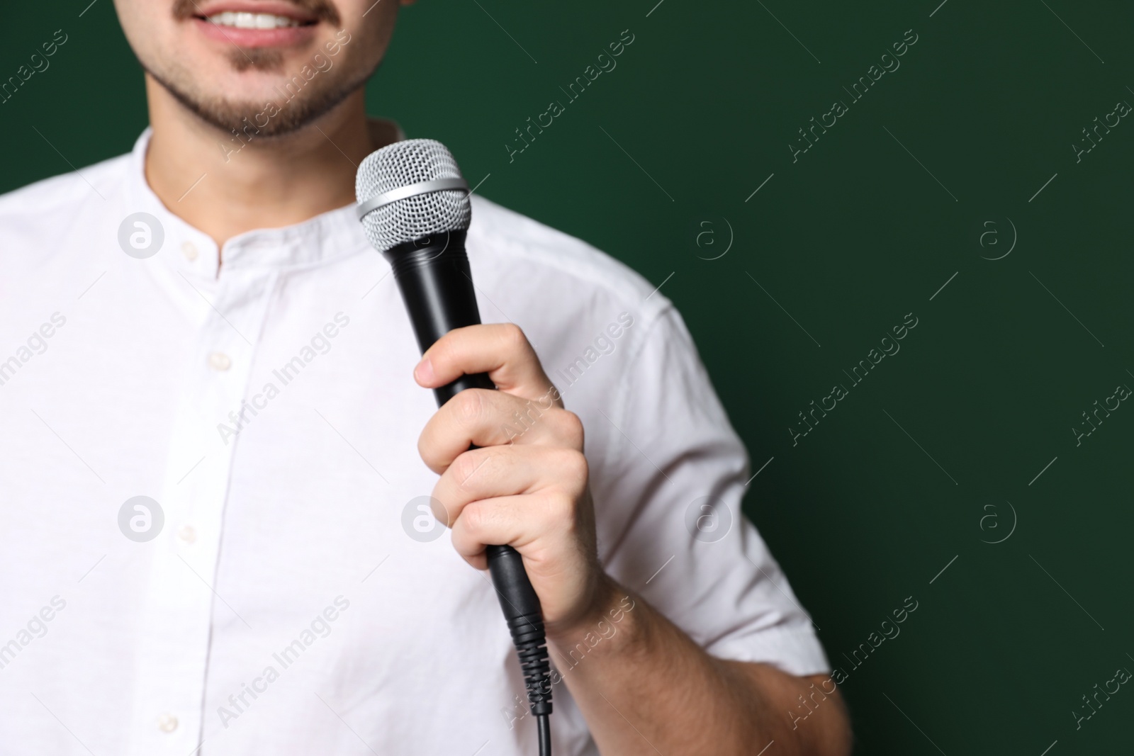 Photo of Young man in casual clothes holding microphone on color background, closeup with space for text