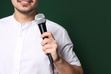 Photo of Young man in casual clothes holding microphone on color background, closeup with space for text