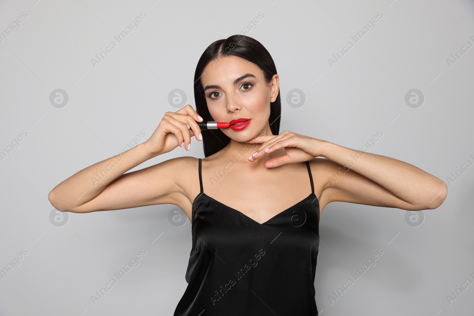 Photo of Young woman with beautiful makeup holding red lipstick on light gray background