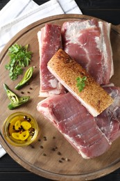 Pieces of raw pork belly, chili pepper, peppercorns, oil and parsley on black wooden table, top view