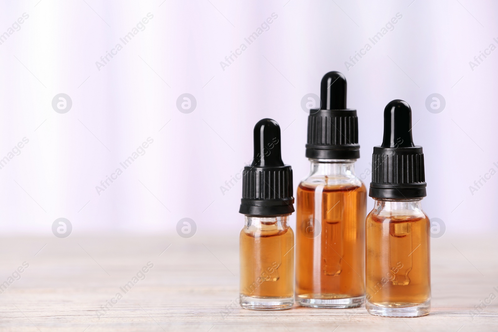 Photo of Bottles of essential oils on table against light background, space for text. Cosmetic products