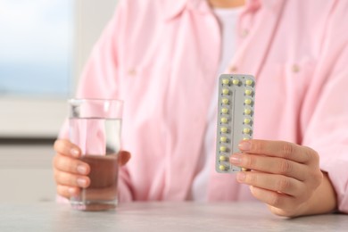 Photo of Woman taking oral contraception pill at light grey table indoors, focus on hand