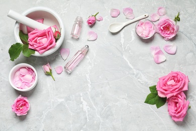 Photo of Flat lay composition with rose essential oil and fresh flowers on grey table, space for text
