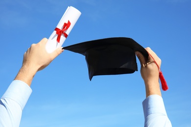 Photo of Student with graduation hat and diploma against blue sky, closeup