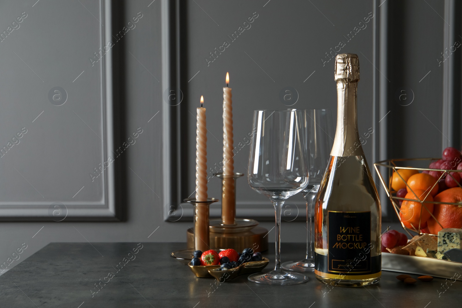 Photo of Bottle of sparkling wine, glasses, candles and delicious snacks on grey table. Space for text