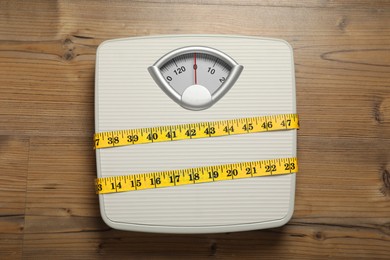 Scales tied with measuring tape on wooden background, top view
