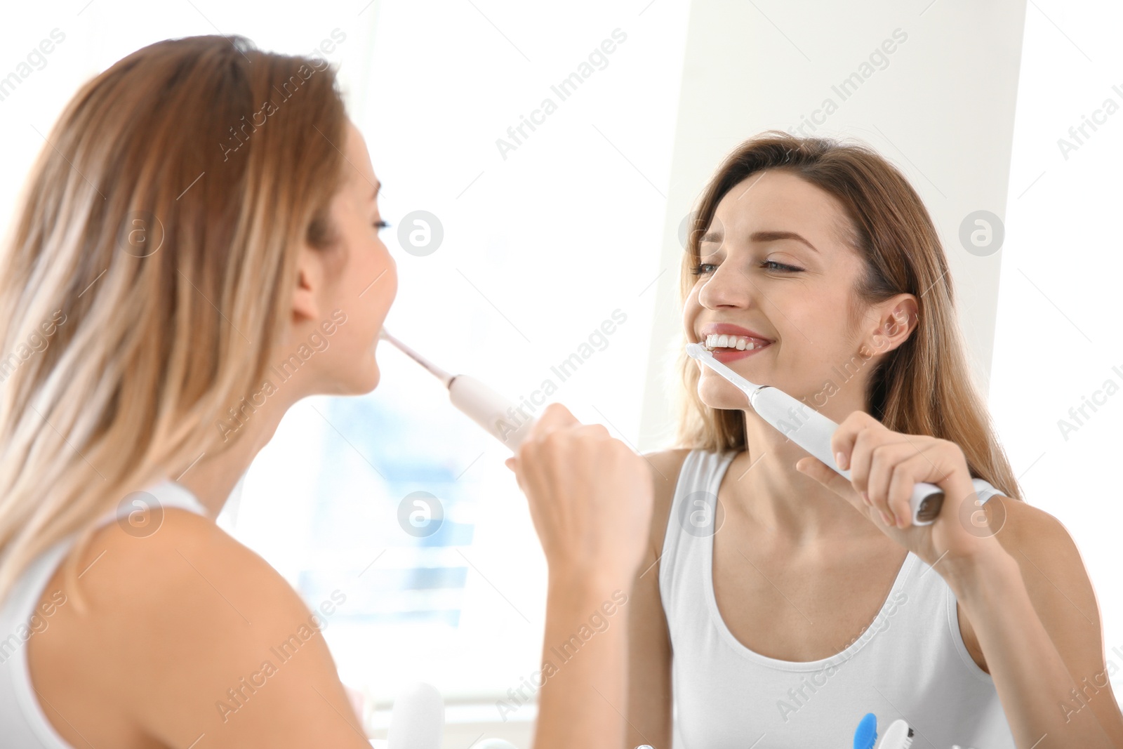 Photo of Young beautiful woman with toothbrush near mirror in bathroom. Personal hygiene