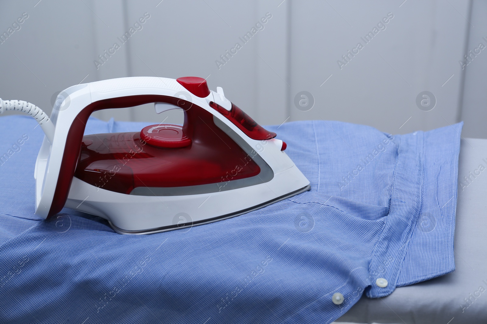 Photo of Modern iron and clean shirt on board indoors