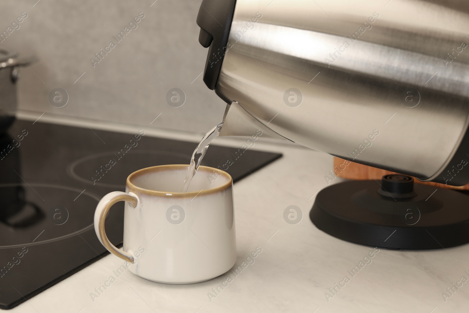 Photo of Pouring hot water from electric kettle into cup in kitchen, closeup