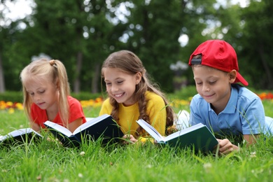 Group of little children reading books on green grass in park