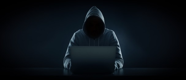 Anonymous man in hood using laptop on black background. Banner design