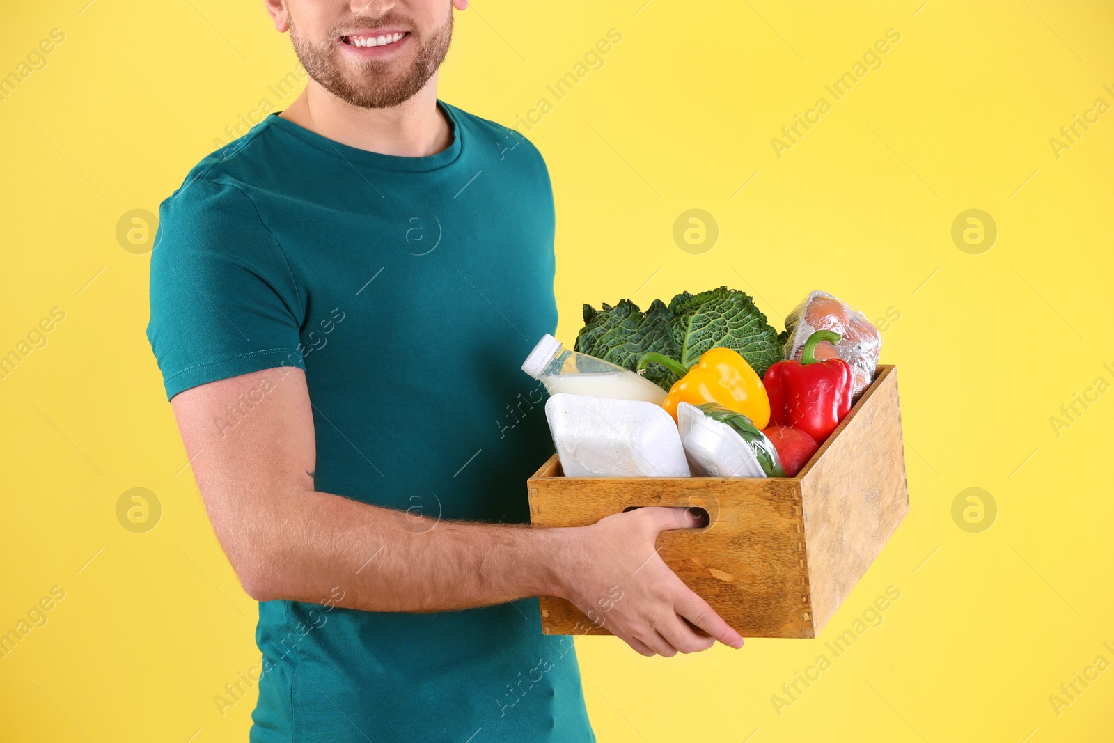 Photo of Delivery man holding wooden crate with food products on color background, closeup