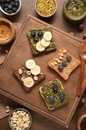Photo of Toasts with different nut butters, blueberries, banana slices and nuts on wooden table, flat lay