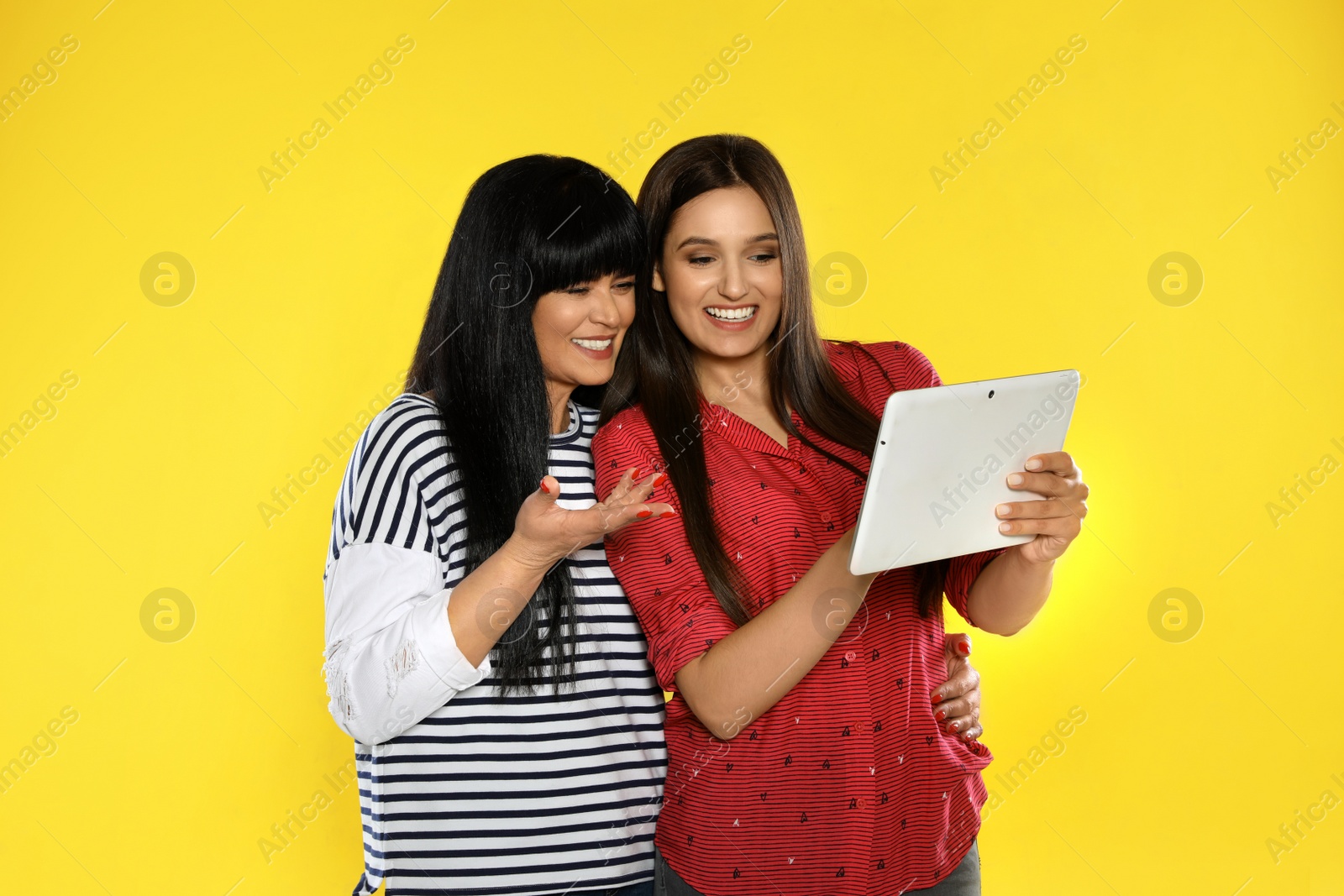 Photo of Young daughter and her mature mother with tablet computer on color background