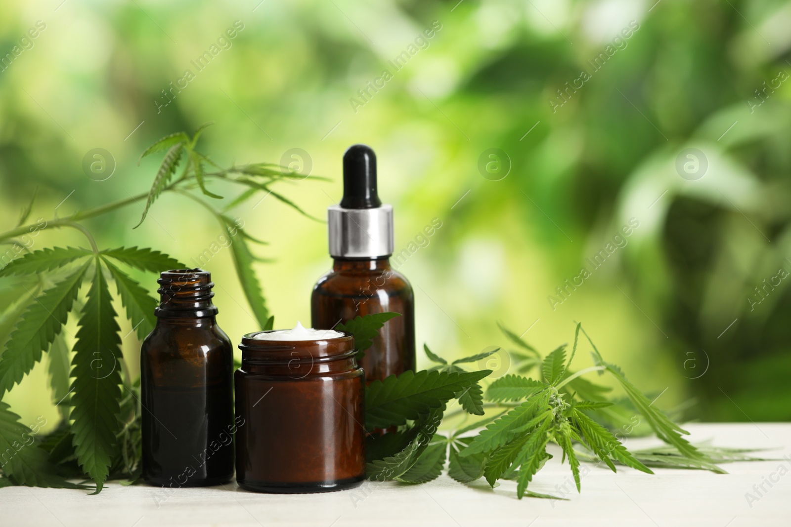 Photo of Cream, hemp leaves, bottles of CBD oil and THC tincture on white wooden table. Space for text