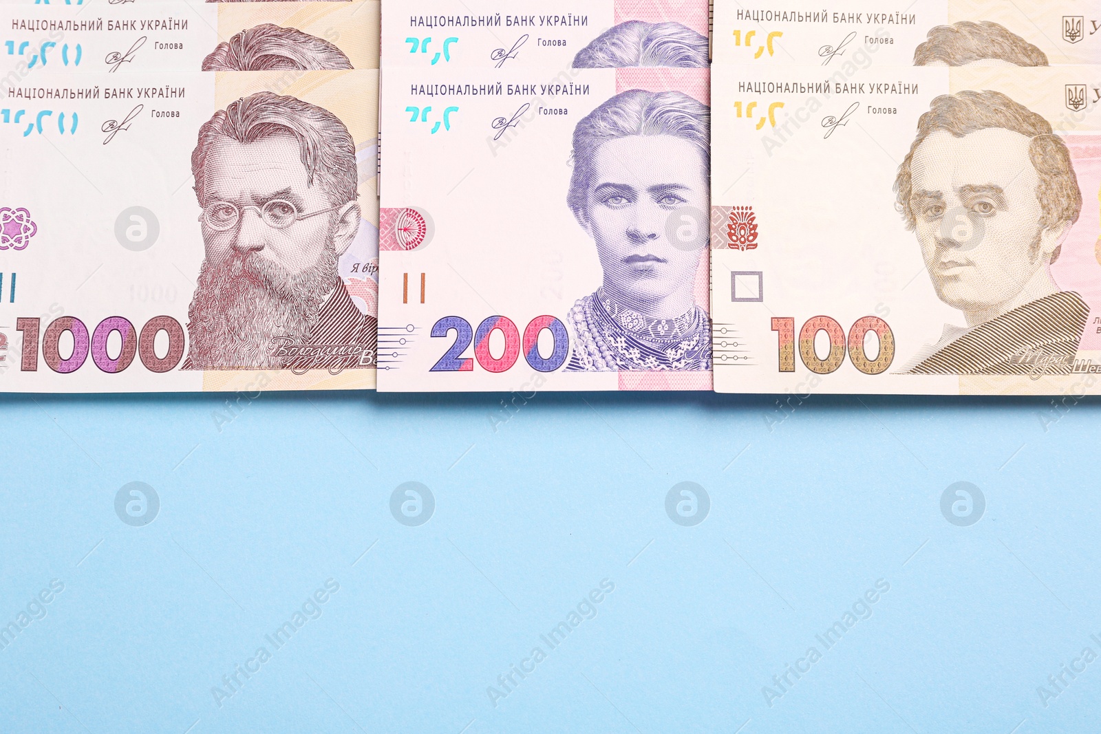 Photo of Ukrainian money on light blue background, flat lay. Space for text