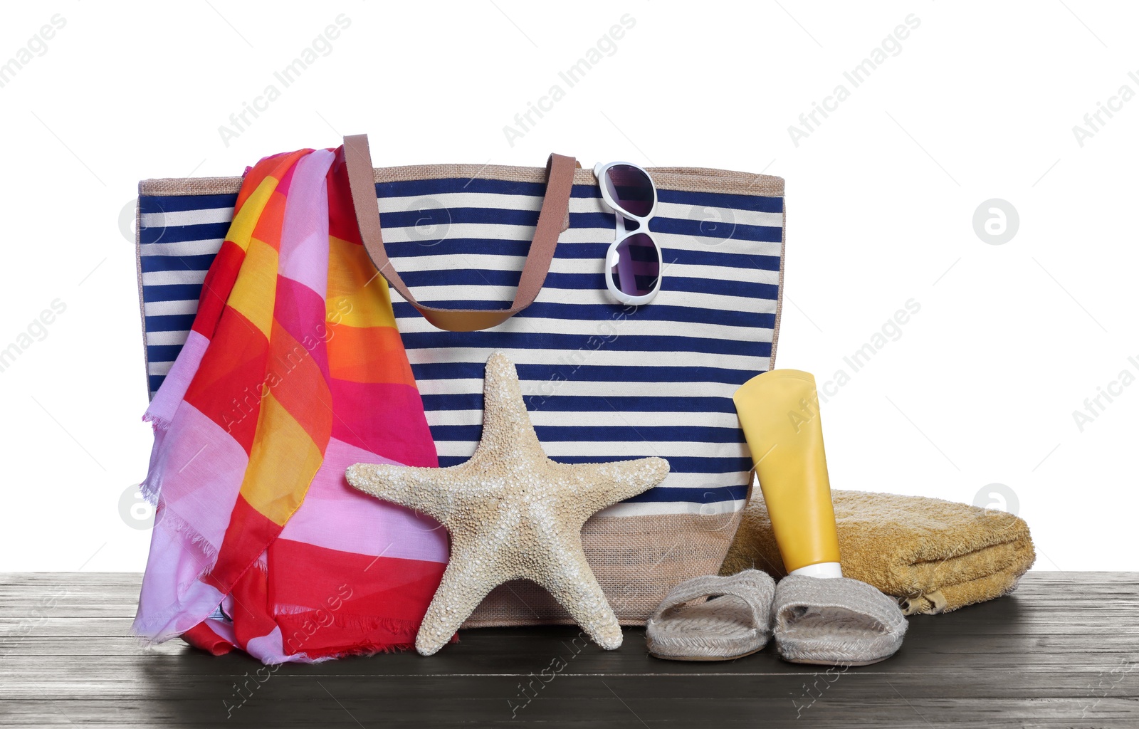 Photo of Stylish bag, starfish and other beach accessories on wooden table against white background