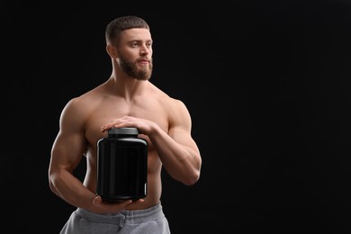 Young man with muscular body holding jar of protein powder on black background, space for text