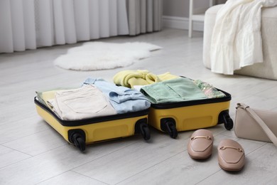 Photo of Open suitcase packed for trip, handbag and shoes on floor indoors