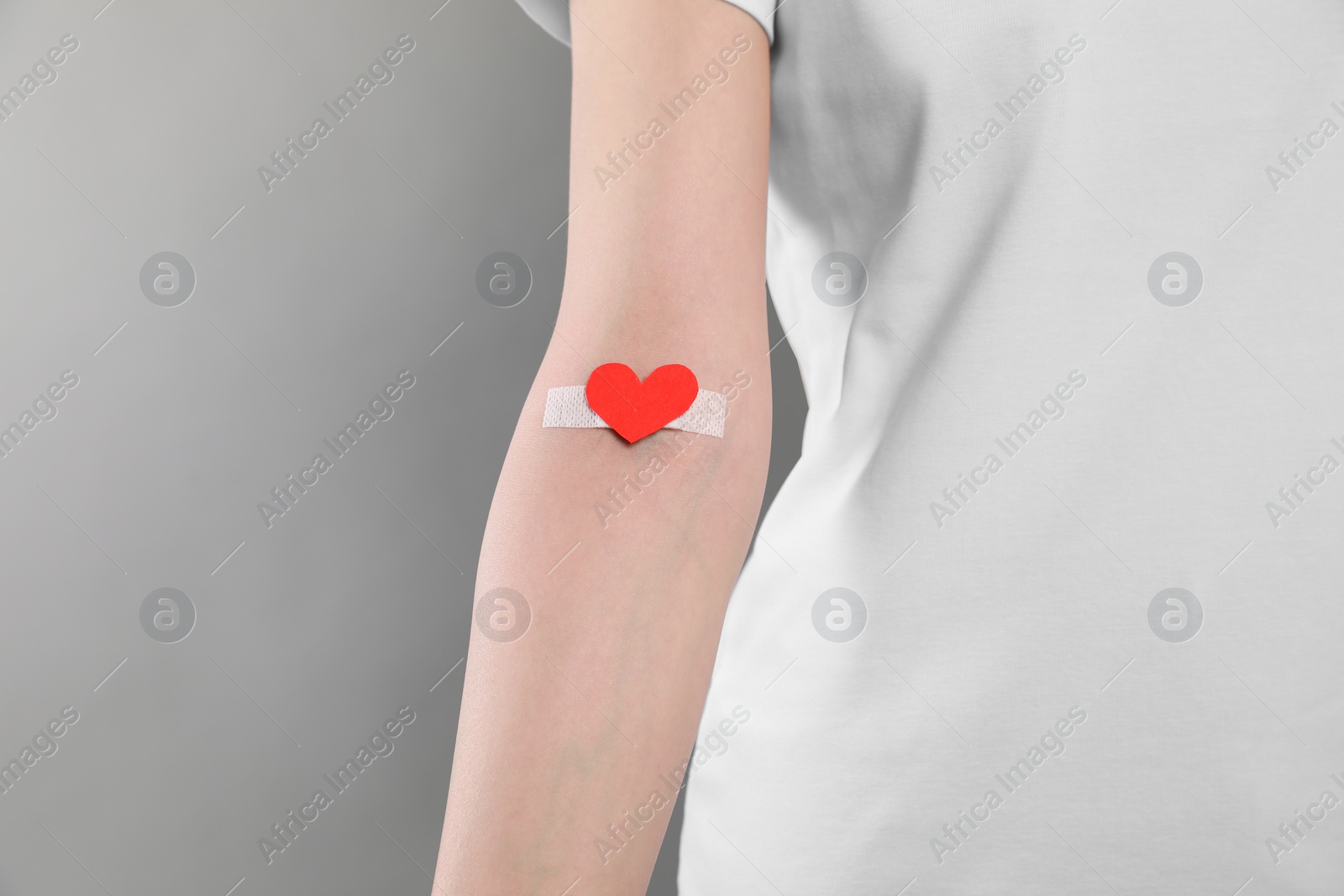 Photo of Blood donation concept. Woman with adhesive plaster on arm against grey background, closeup. Space for text