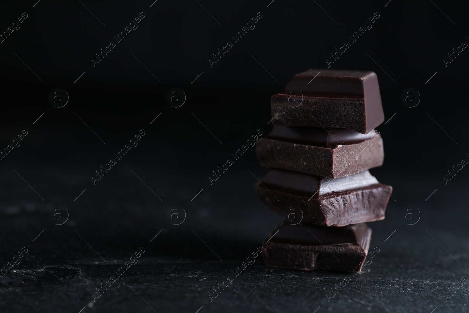 Photo of Delicious dark chocolate on black table. Space for text