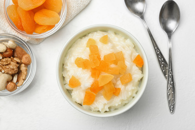 Photo of Delicious rice pudding with dried apricots on white table, flat lay