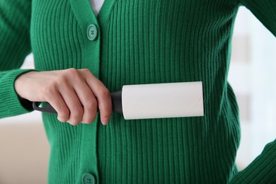 Woman cleaning green jacket with lint roller on light background, closeup