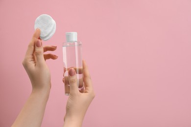 Photo of Woman holding makeup remover and cotton pads on pink background, closeup. Space for text