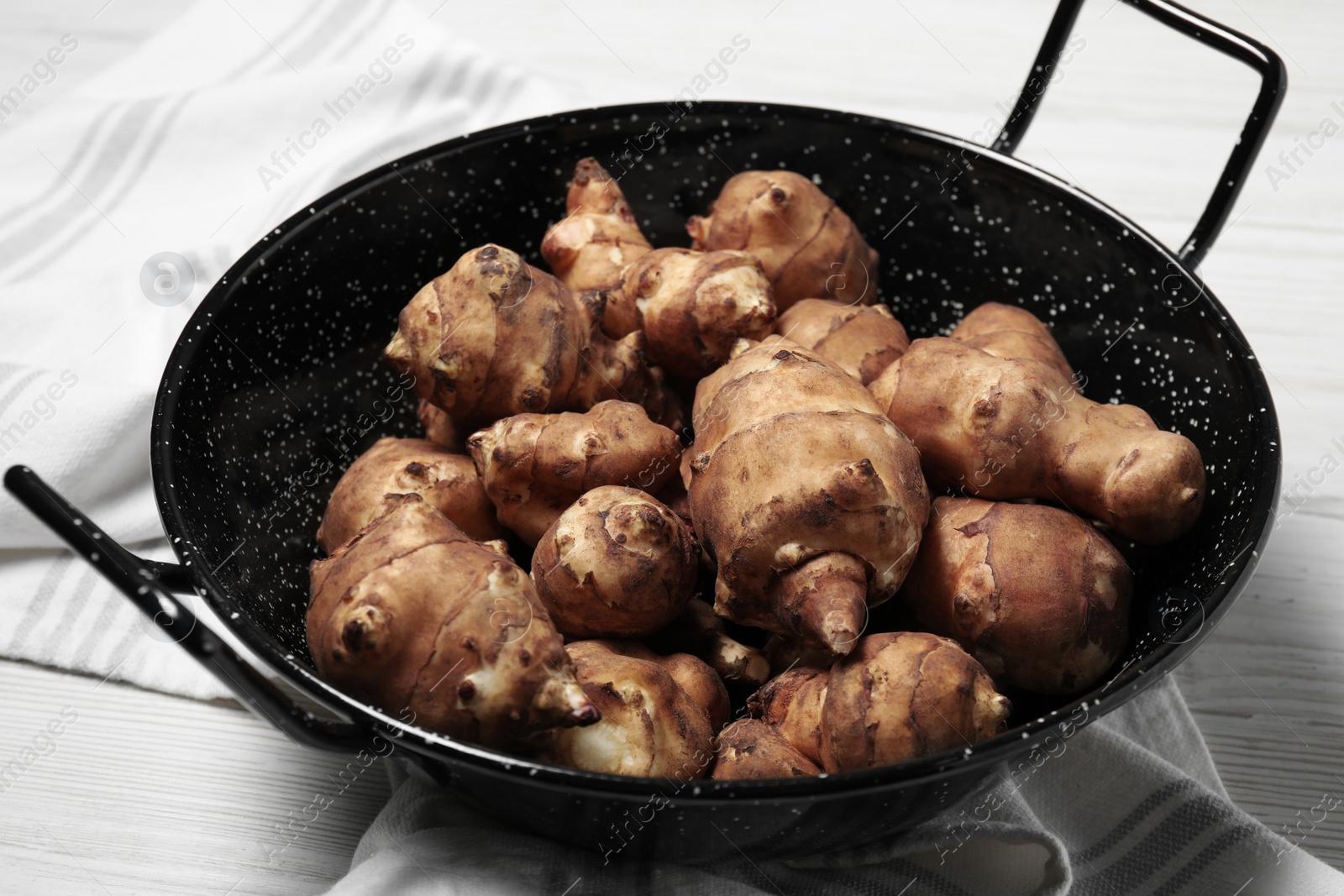 Photo of Pan with fresh Jerusalem artichokes on white wooden table, closeup