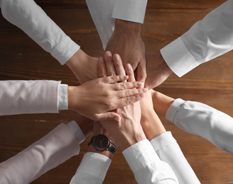 Photo of People holding hands together over wooden background, top view. Unity concept