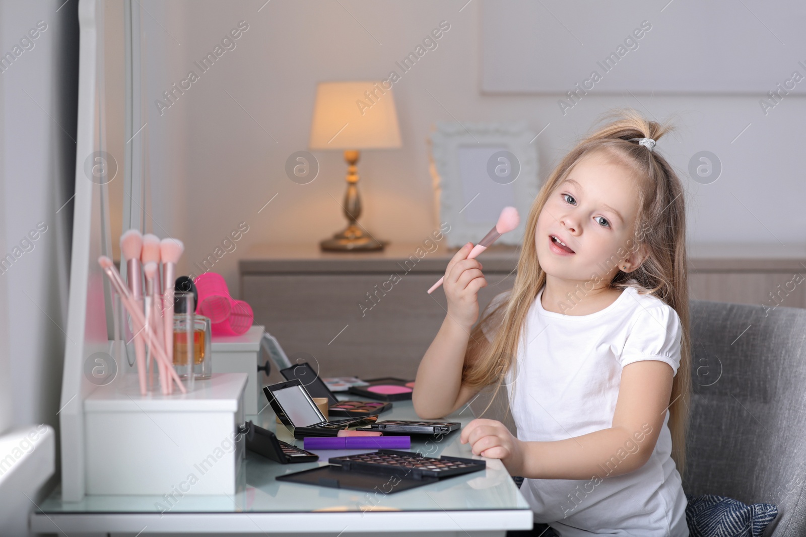 Photo of Adorable little girl applying makeup at dressing table indoors