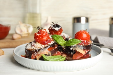 Baked eggplant with tomatoes, cheese and basil served on white wooden table