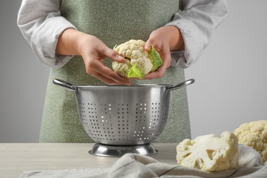 Photo of Woman separating fresh cauliflower cabbage above colander at wooden table, closeup