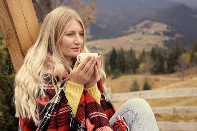 Young woman with cup of hot drink in mountains. Space for text