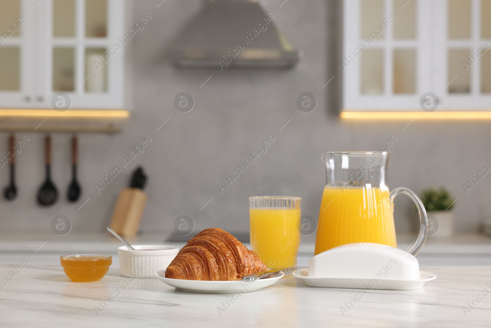 Photo of Breakfast served in kitchen. Fresh croissant, jam, honey and orange juice on white table