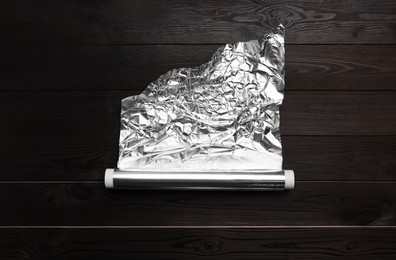 Photo of Roll of aluminum foil on dark wooden table, top view