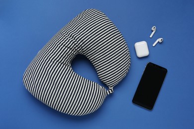 Photo of Striped travel pillow, smartphone and earphones on blue background, flat lay